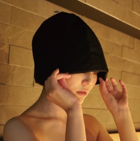 베이지 타일 사우나에서 검정 사우나 모자의 가장자리를 양손으로 조절하는 사람